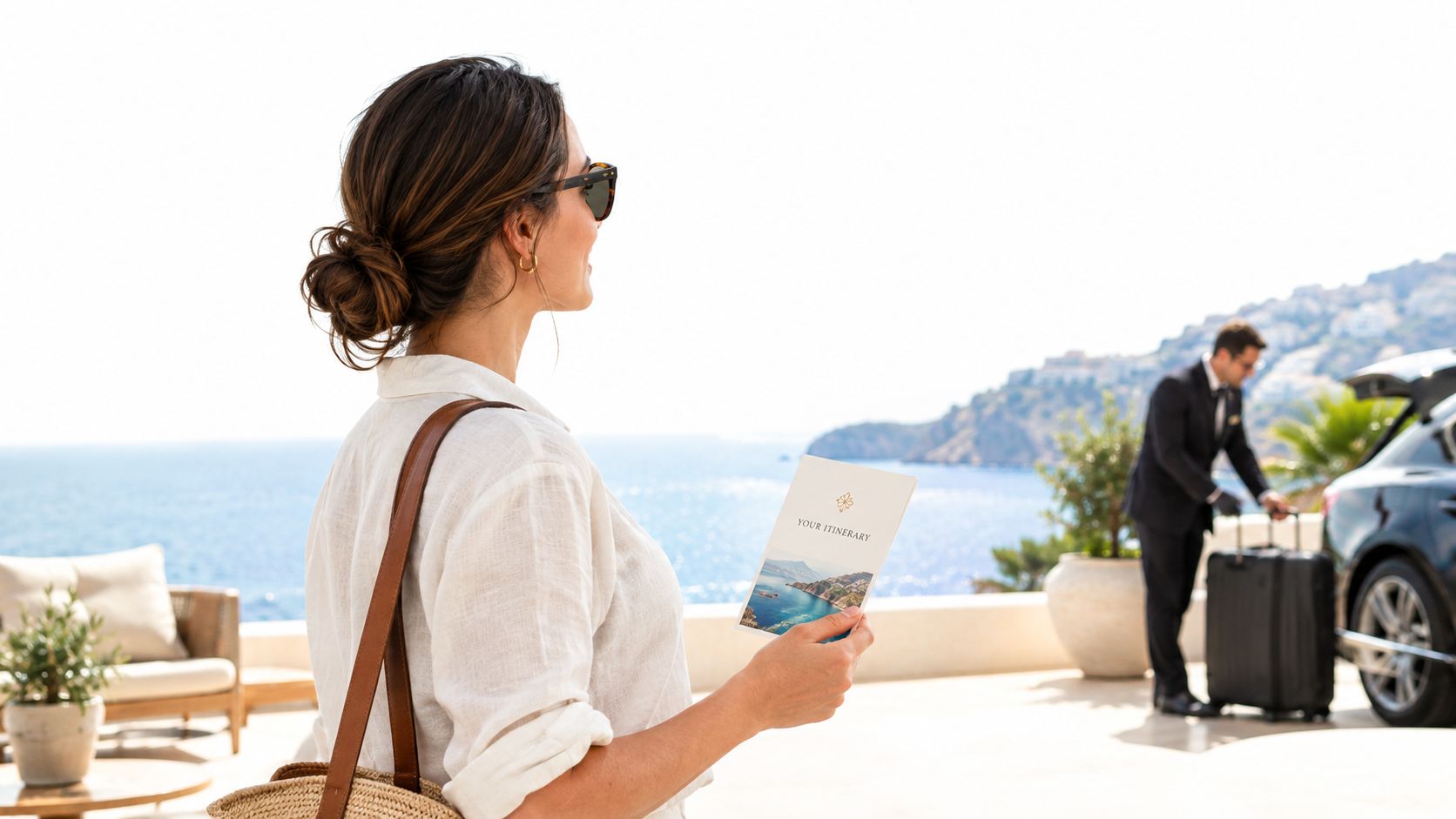 A woman holding a travel itinerary brochure overlooking a scenic coastal view with a chauffeur nearby.
