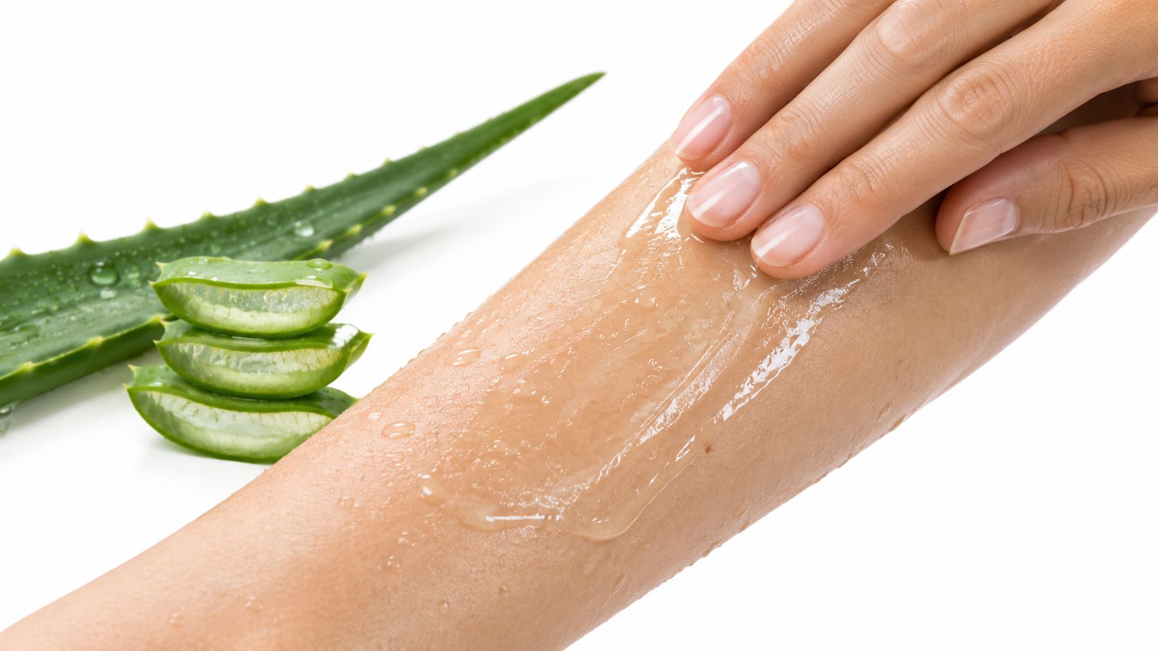 A close-up view of aloe vera gel being applied to a person's arm with aloe slices nearby.