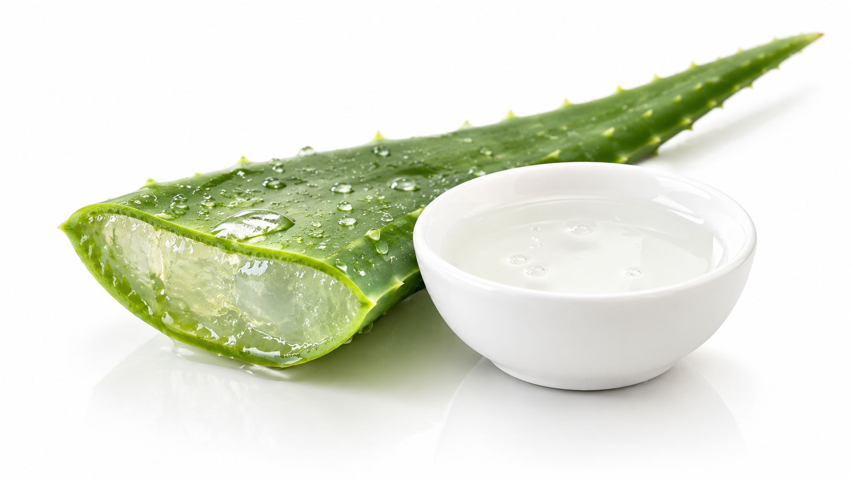 A fresh aloe vera leaf with water droplets next to a small white bowl of clear gel.