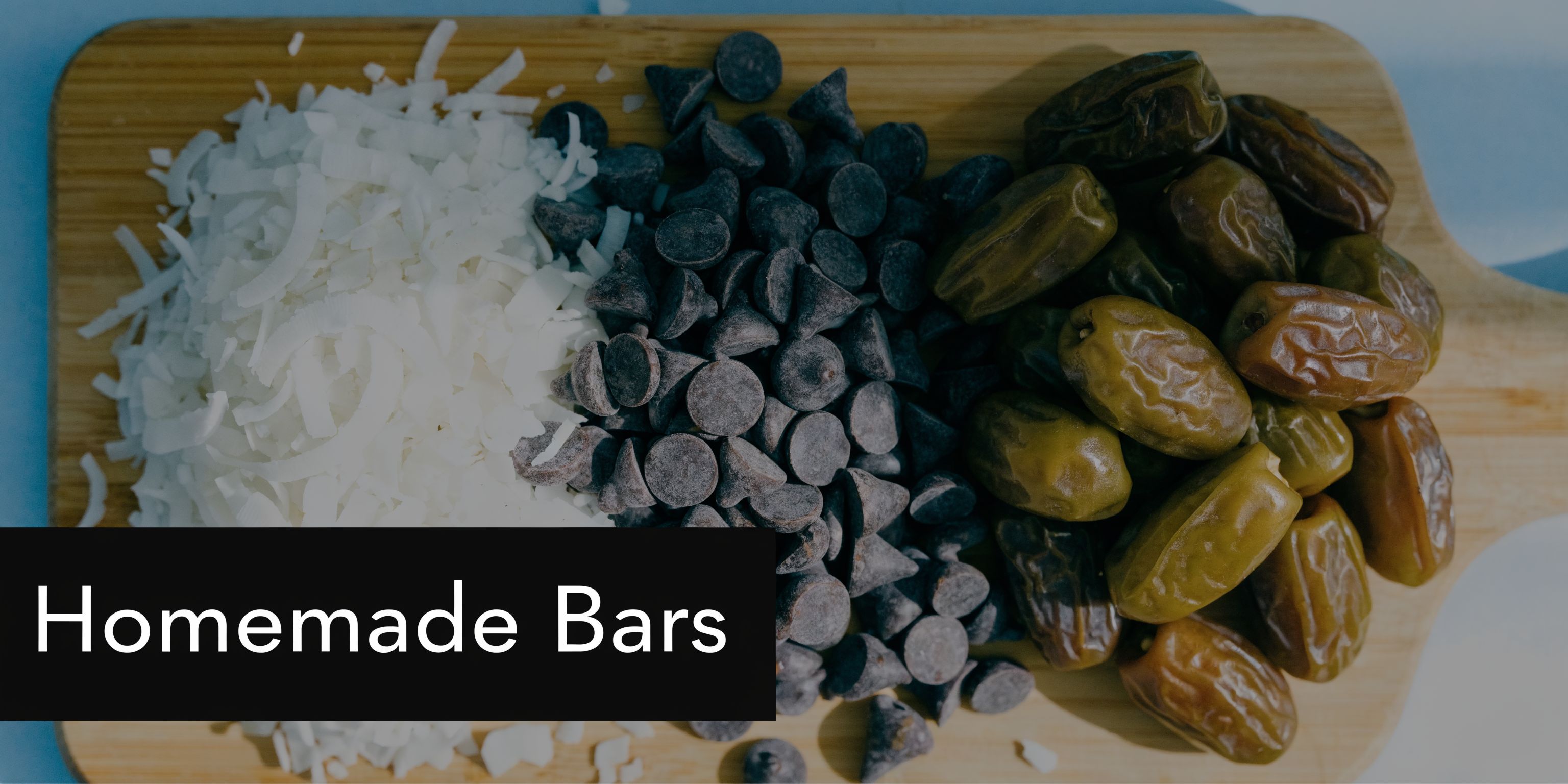 A wooden cutting board with a pile of shredded coconut, dark chocolate chips, and whole pitted dates.