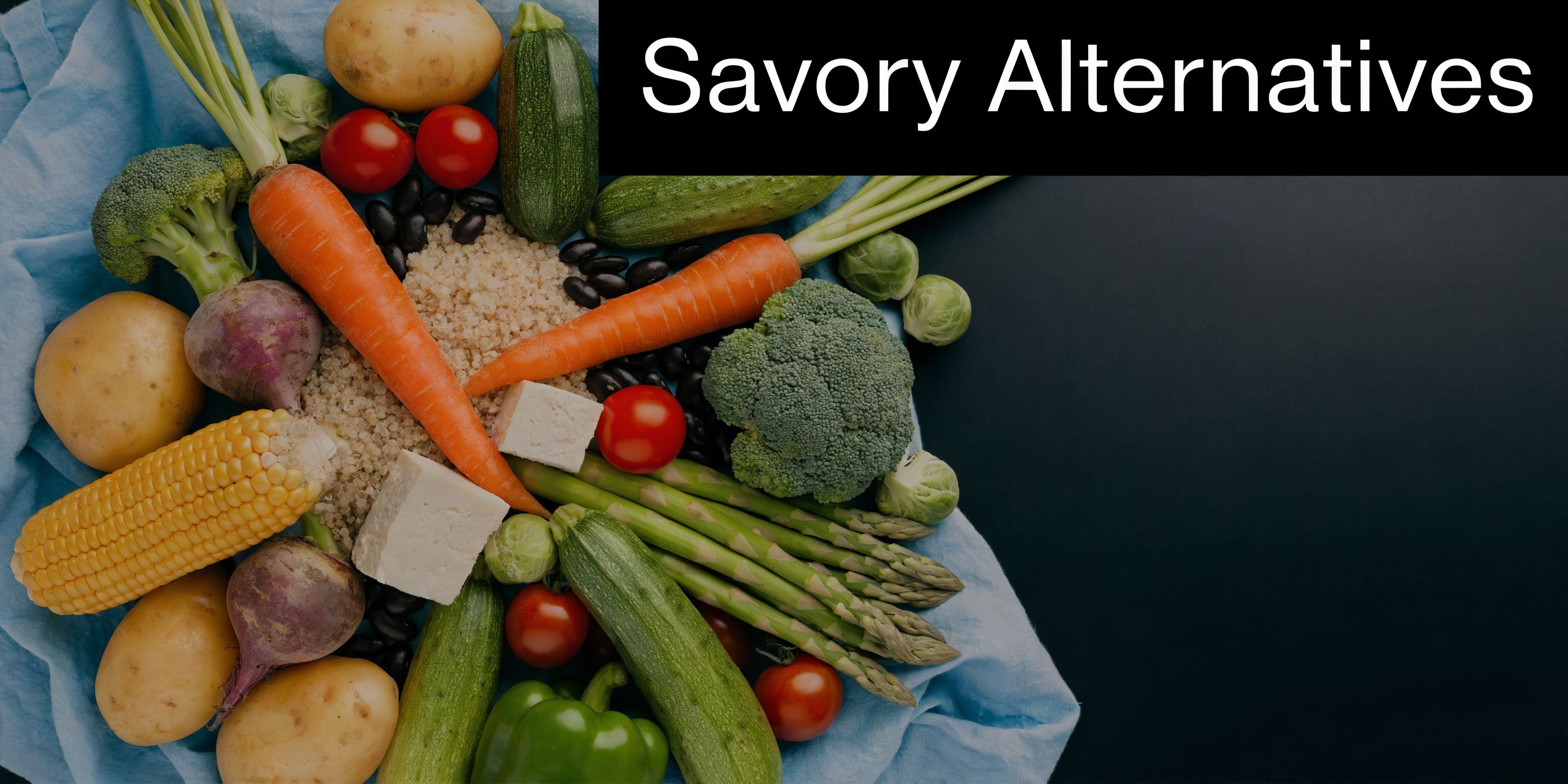An assortment of fresh vegetables, grains, and tofu arranged on a blue cloth with black background.