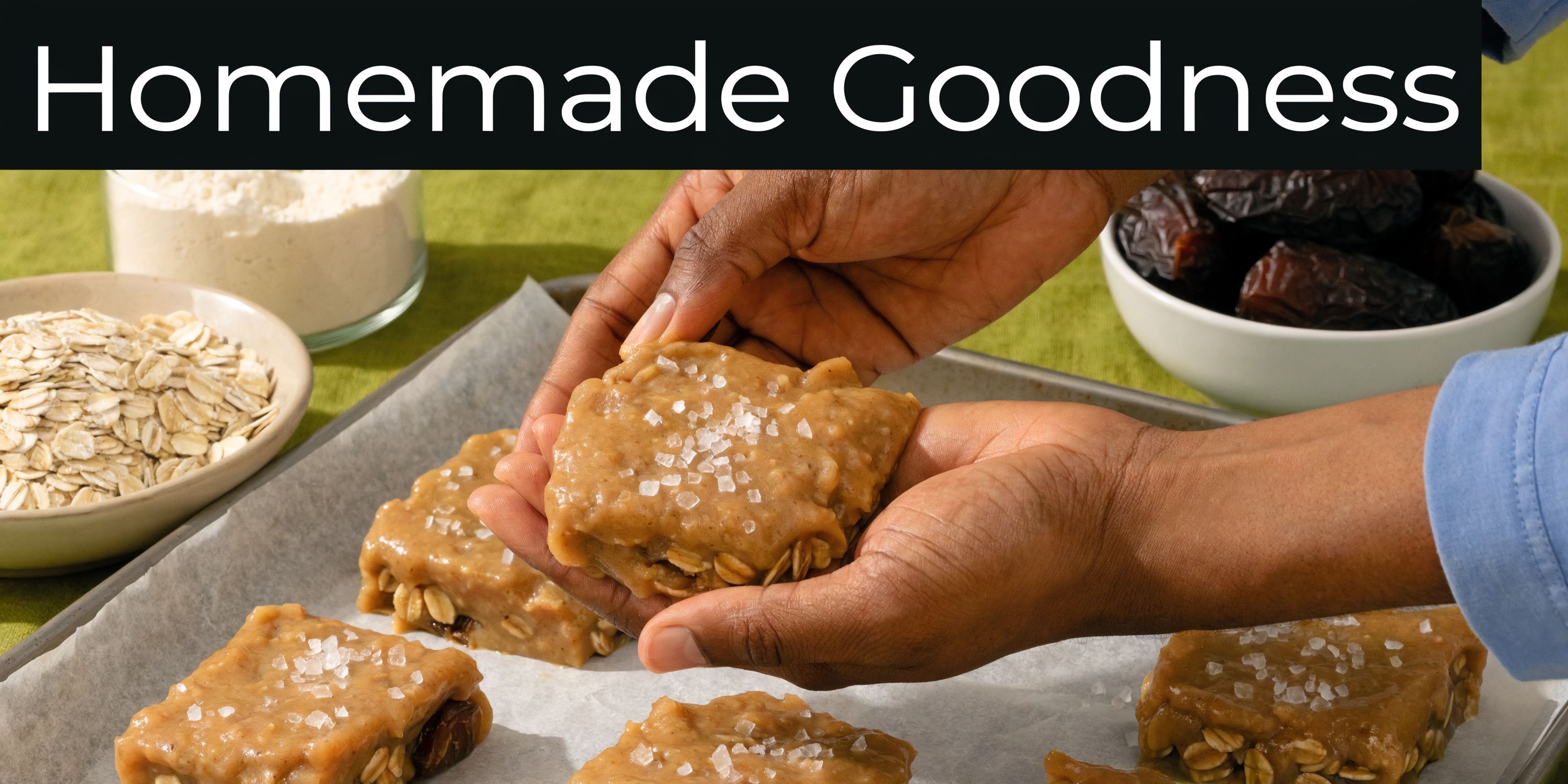 A person holding a square homemade salted caramel protein bar topped with sea salt flakes over a tray.