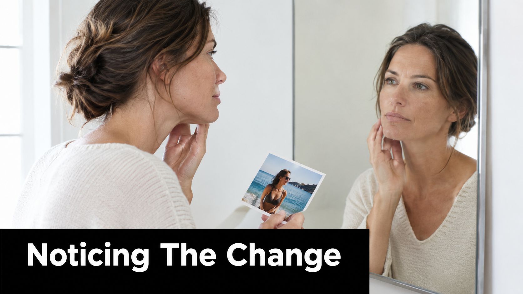 A woman looks at an older photo of herself in a mirror, reflecting on aging and changing skin.