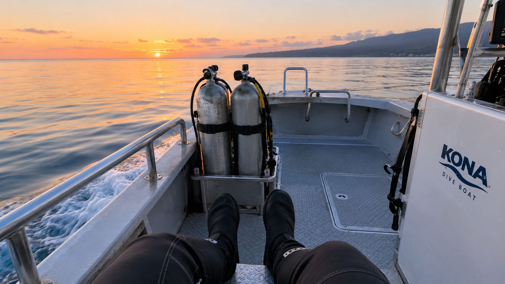 A person wearing a wetsuit sits on a Kona dive boat facing the sunset over the ocean.