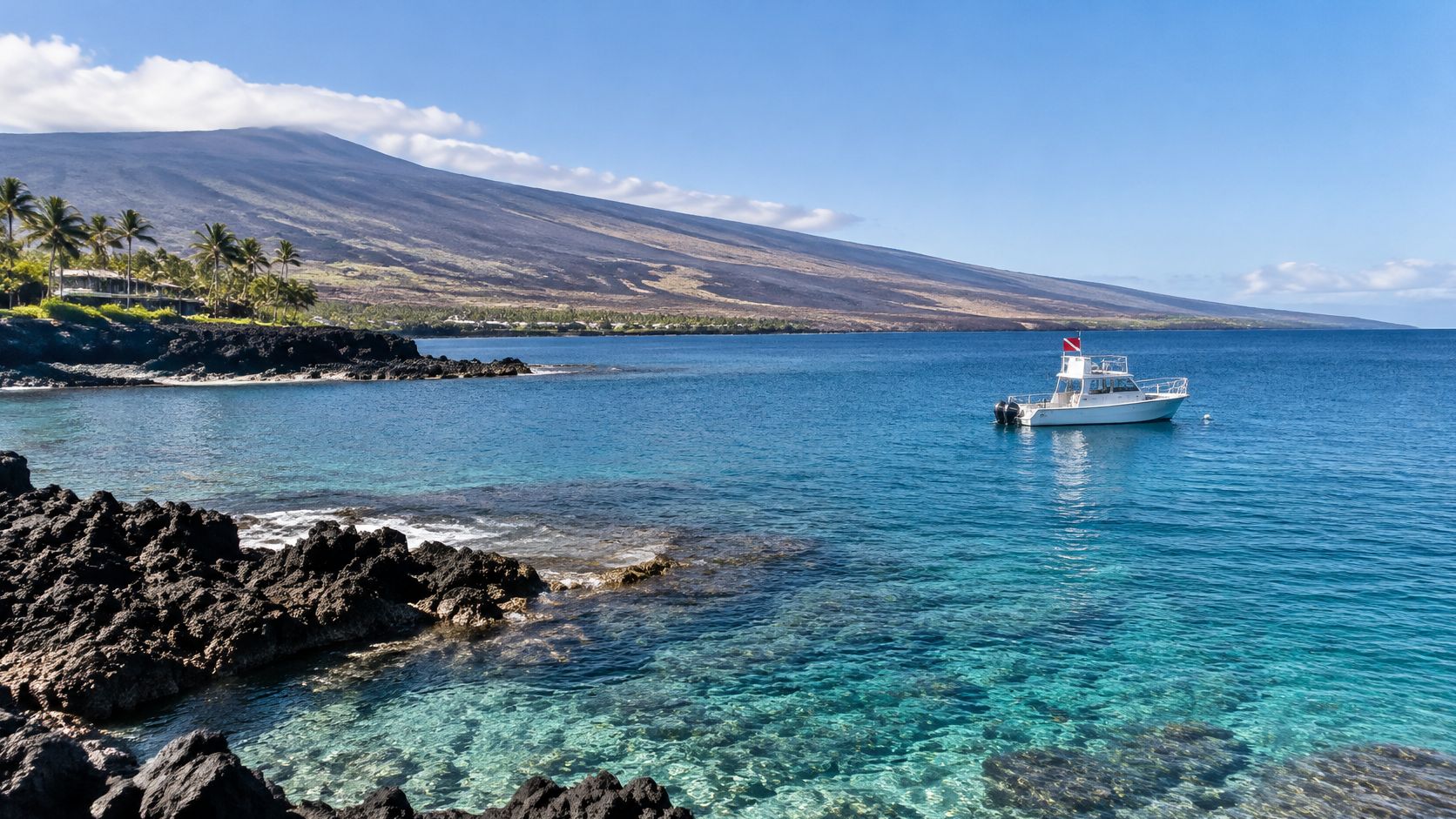 A white dive boat floating on the turquoise waters near the rocky lava coastline of Kona Hawaii.