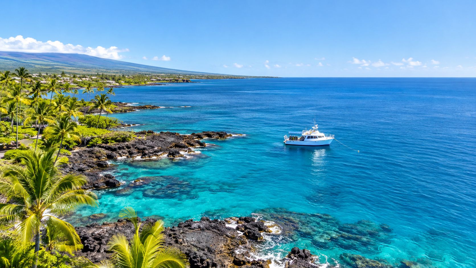 A white tour boat anchored in the crystal clear turquoise waters off the rocky Big Island coastline.