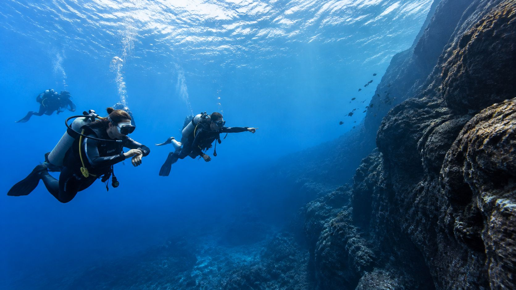 Scuba divers exploring the clear blue underwater terrain off the coast of Kona, Hawaii.