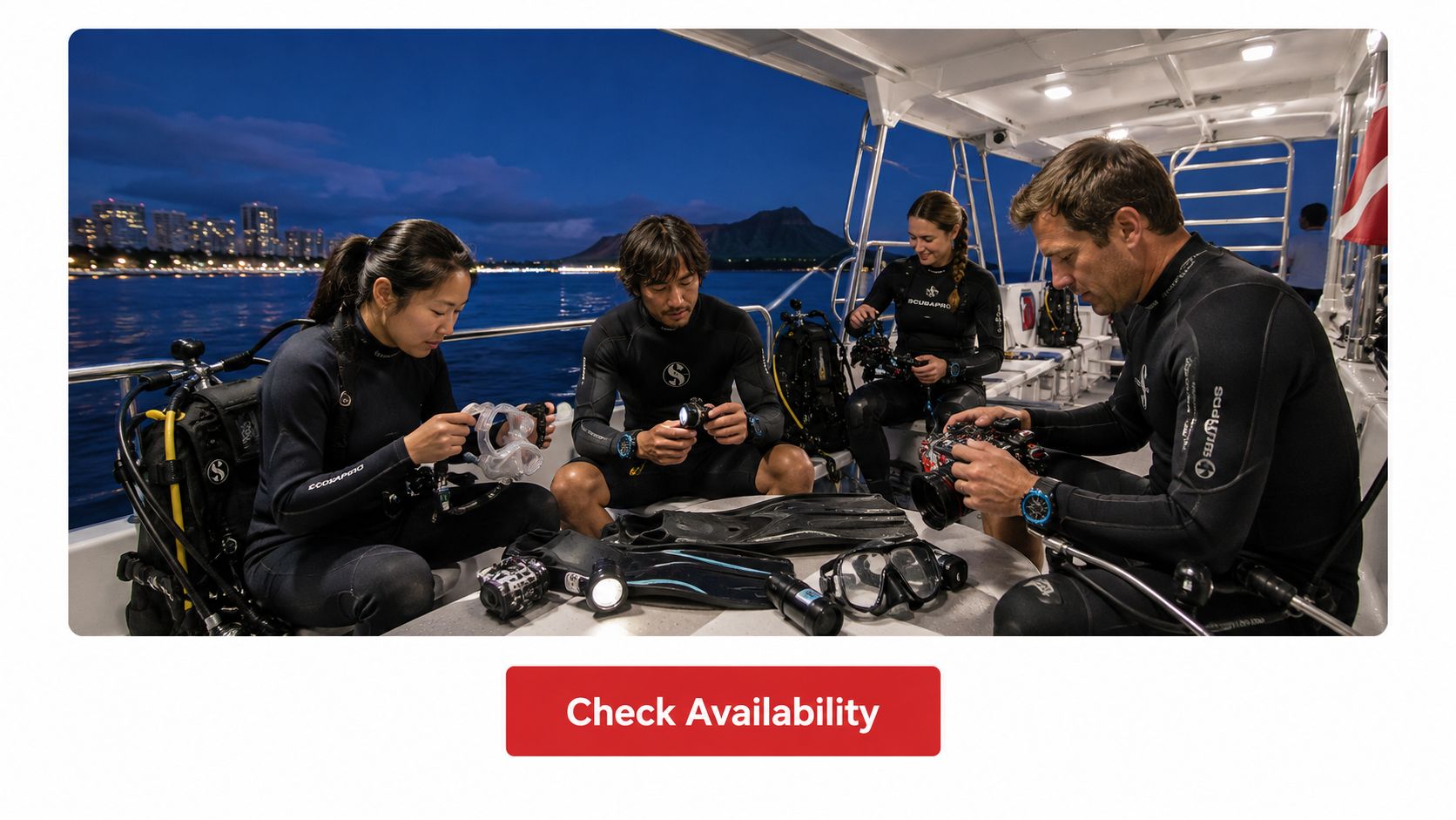 Scuba divers preparing gear on a boat at night with the Honolulu city skyline in the background.