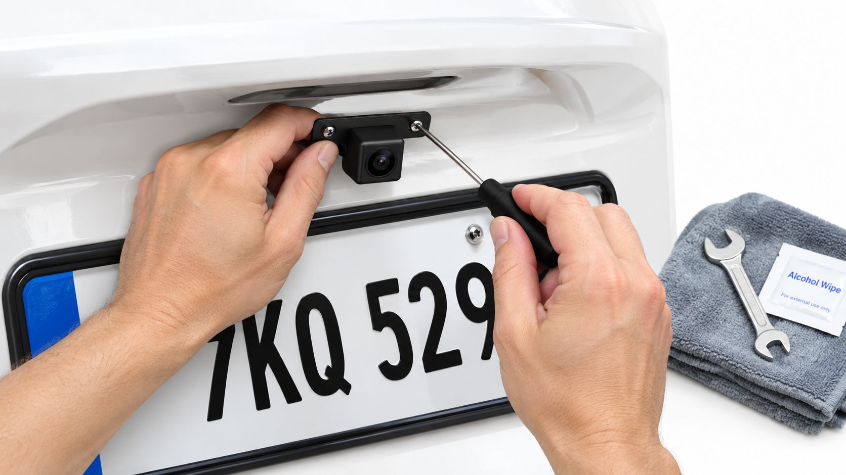 A person uses a screwdriver to install a small license plate mount backup camera on a car.