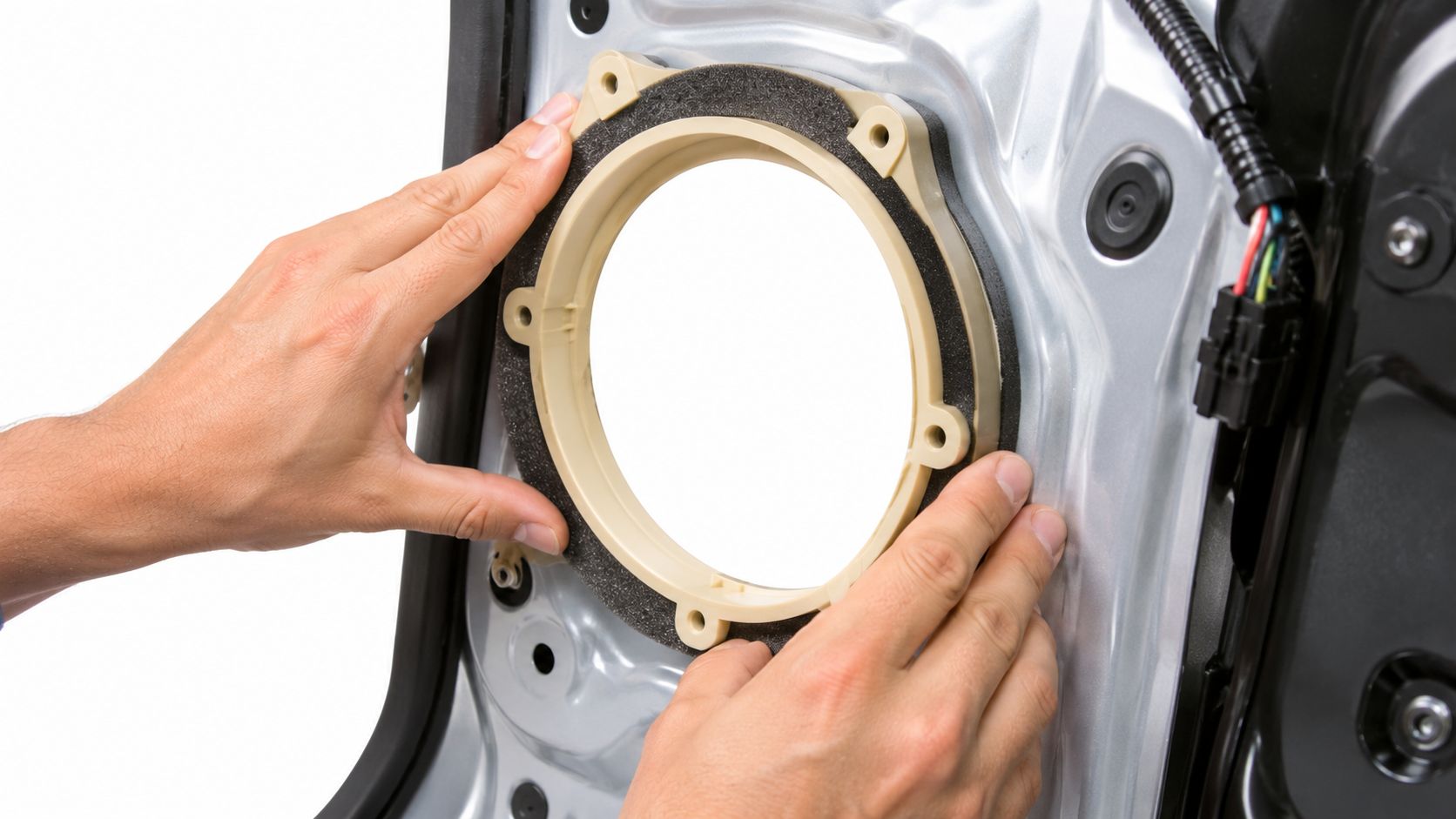 Hands positioning a plastic speaker adapter ring onto a vehicle's metal car door frame.