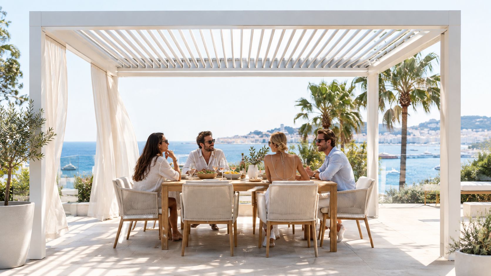 Quatre amis profitent d'un déjeuner ensoleillé sous une pergola bioclimatique électrique moderne avec vue sur la mer.