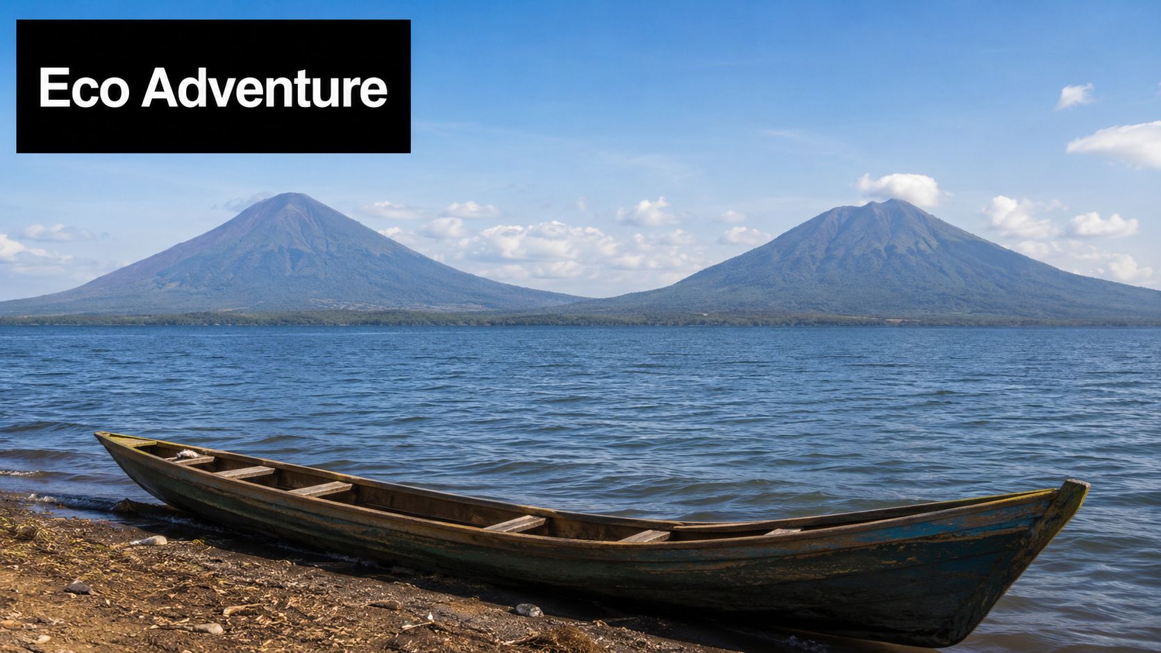 A wooden boat rests on the shore of a lake with two large volcanoes in the background.
