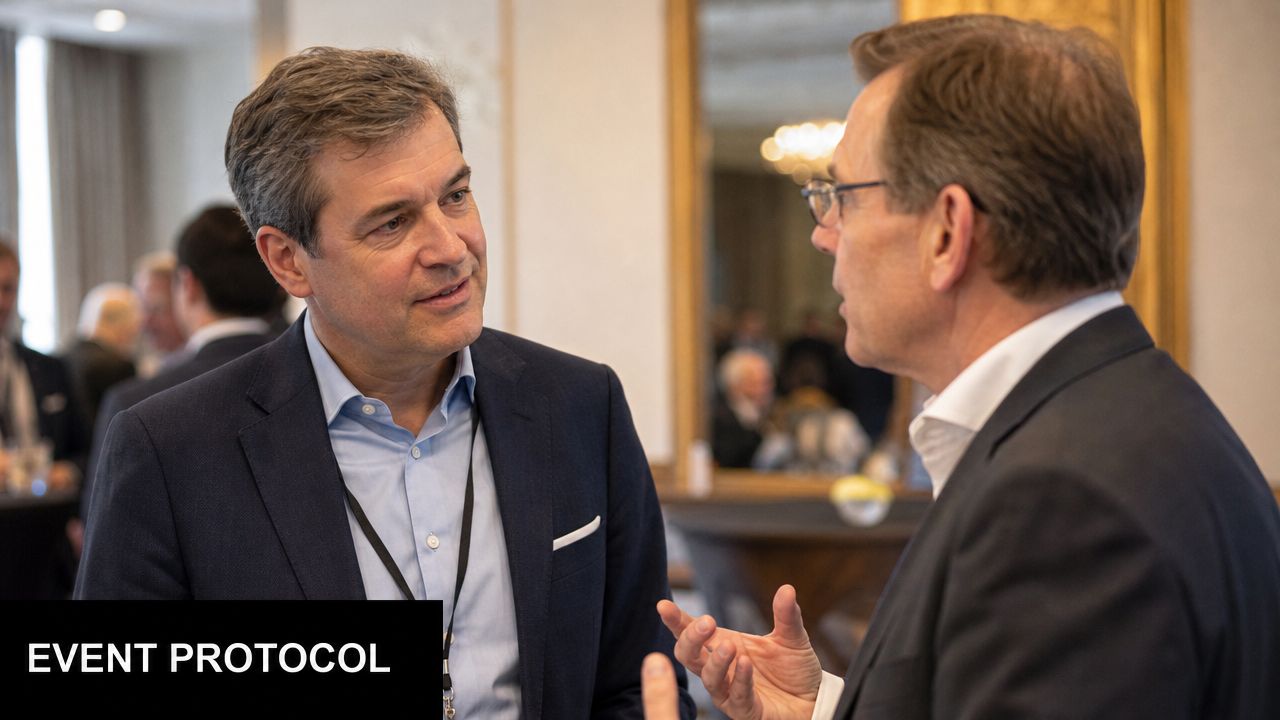 Two middle-aged men in suits engaged in professional conversation during an executive networking event indoors.