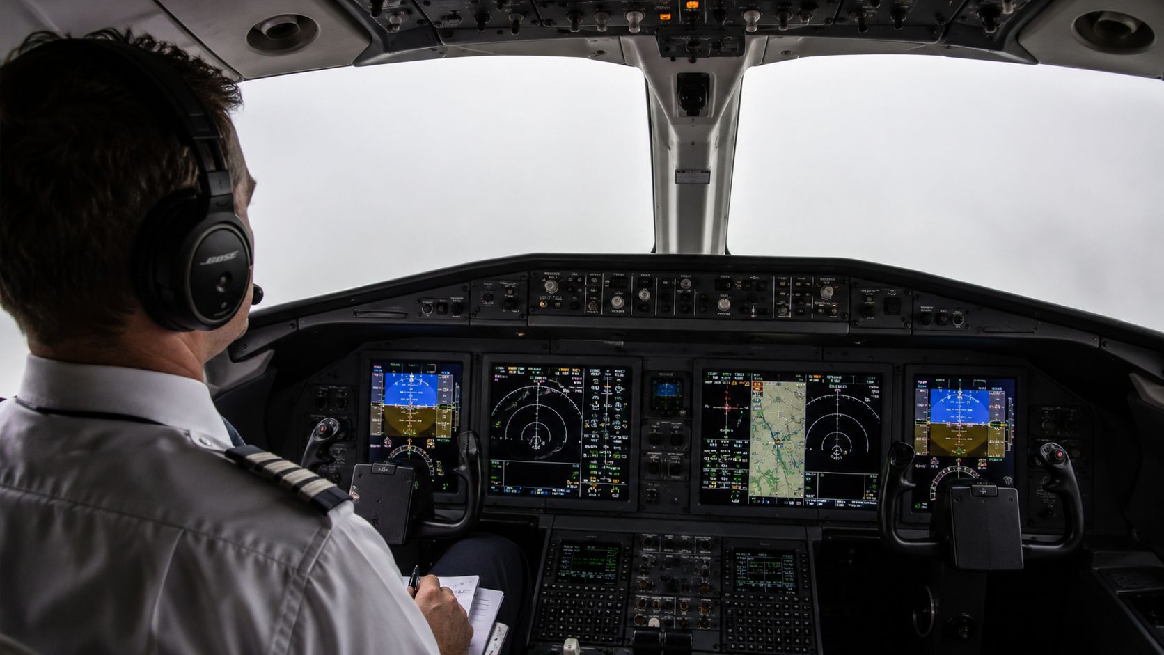A pilot wearing a headset works in a modern airplane cockpit under instrument meteorological conditions.