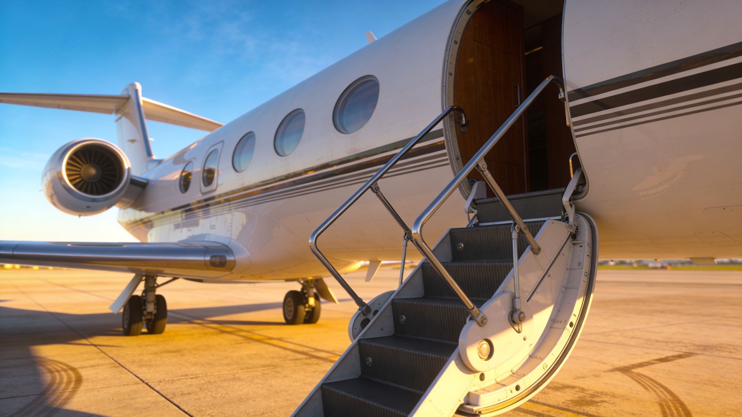 A luxurious private jet parked on an airport tarmac with stairs deployed for boarding at sunset.