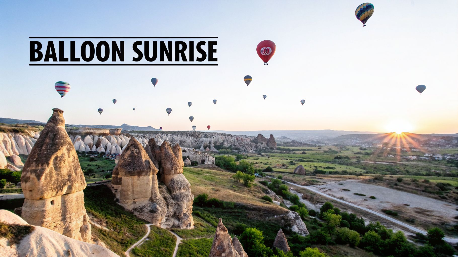 Hot air balloons float above unique rock formations and green valleys during a beautiful sunrise in Cappadocia.