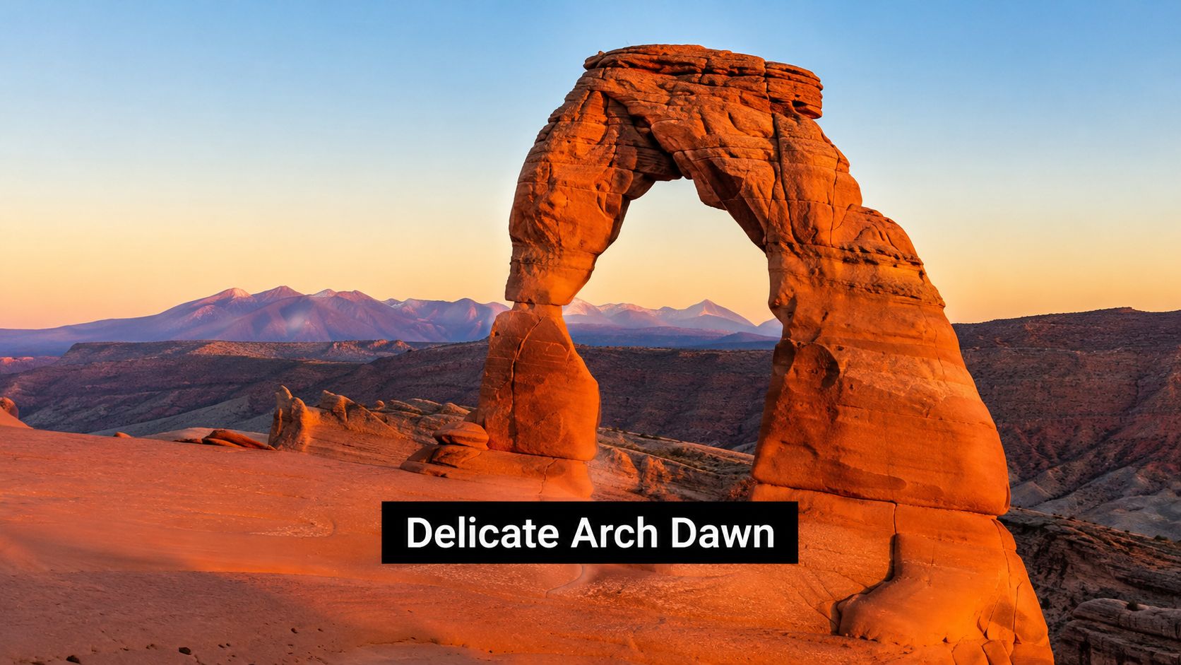 The iconic Delicate Arch stands against a beautiful orange sunrise in Arches National Park, Utah.