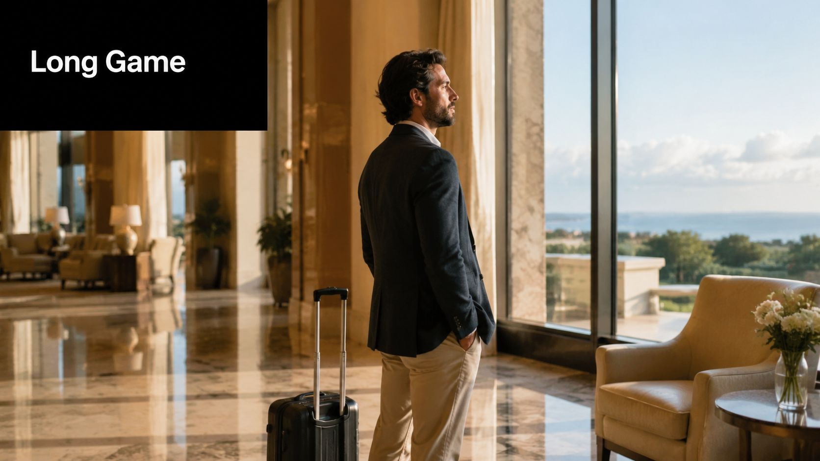 A businessman standing in a luxurious hotel lobby looking out a large window at a scenic view.