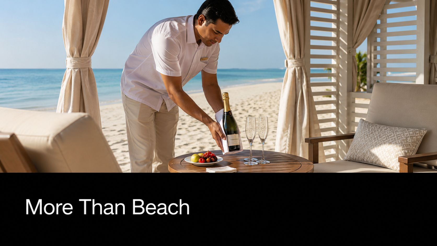A hotel butler serves a chilled bottle of champagne and fresh fruit in a luxury beach cabana.