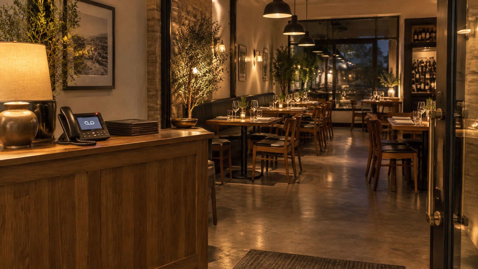 A warm, dimly lit restaurant entrance featuring a wooden host desk with a telephone and phone system.