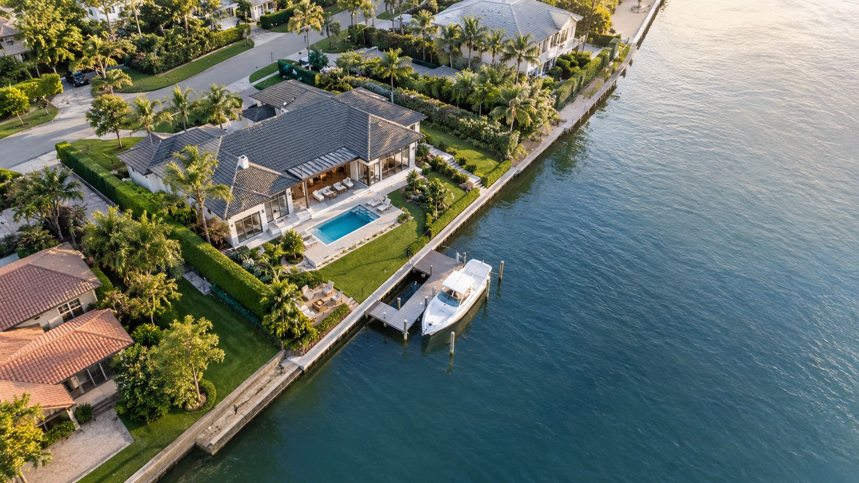 A luxurious waterfront home featuring a private pool and a boat docked on a canal at sunset.