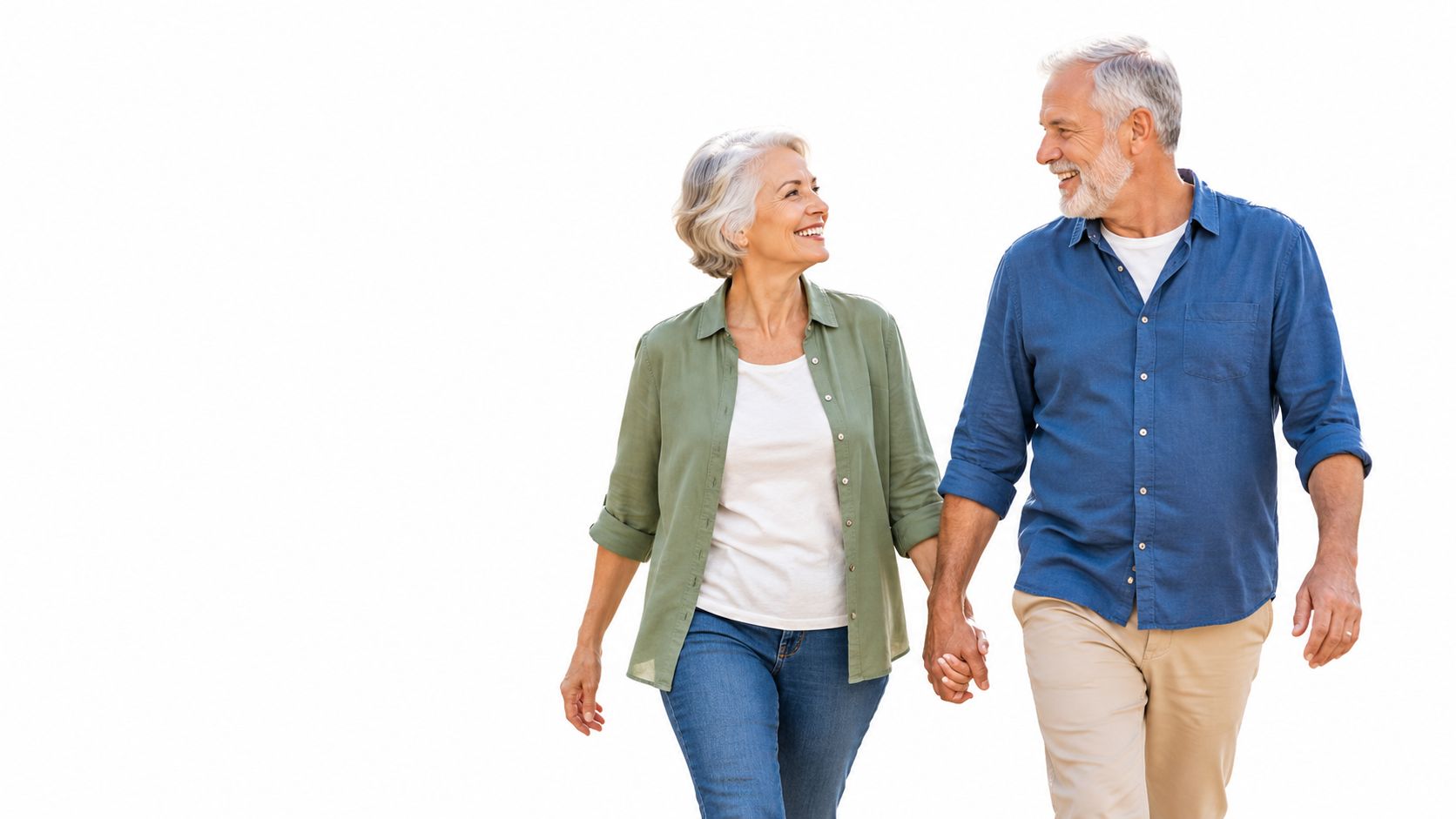 A happy senior couple walking hand in hand, looking at each other, isolated on a white background.