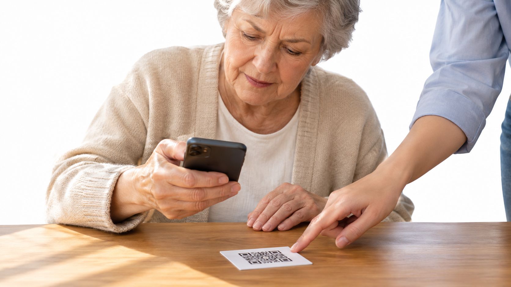 An older woman being guided by another person to scan a QR code with her smartphone.