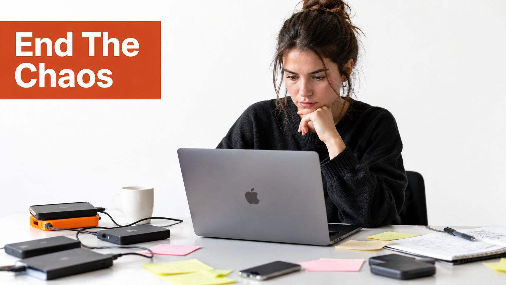 A woman working on a laptop at a desk cluttered with multiple external hard drives and papers.