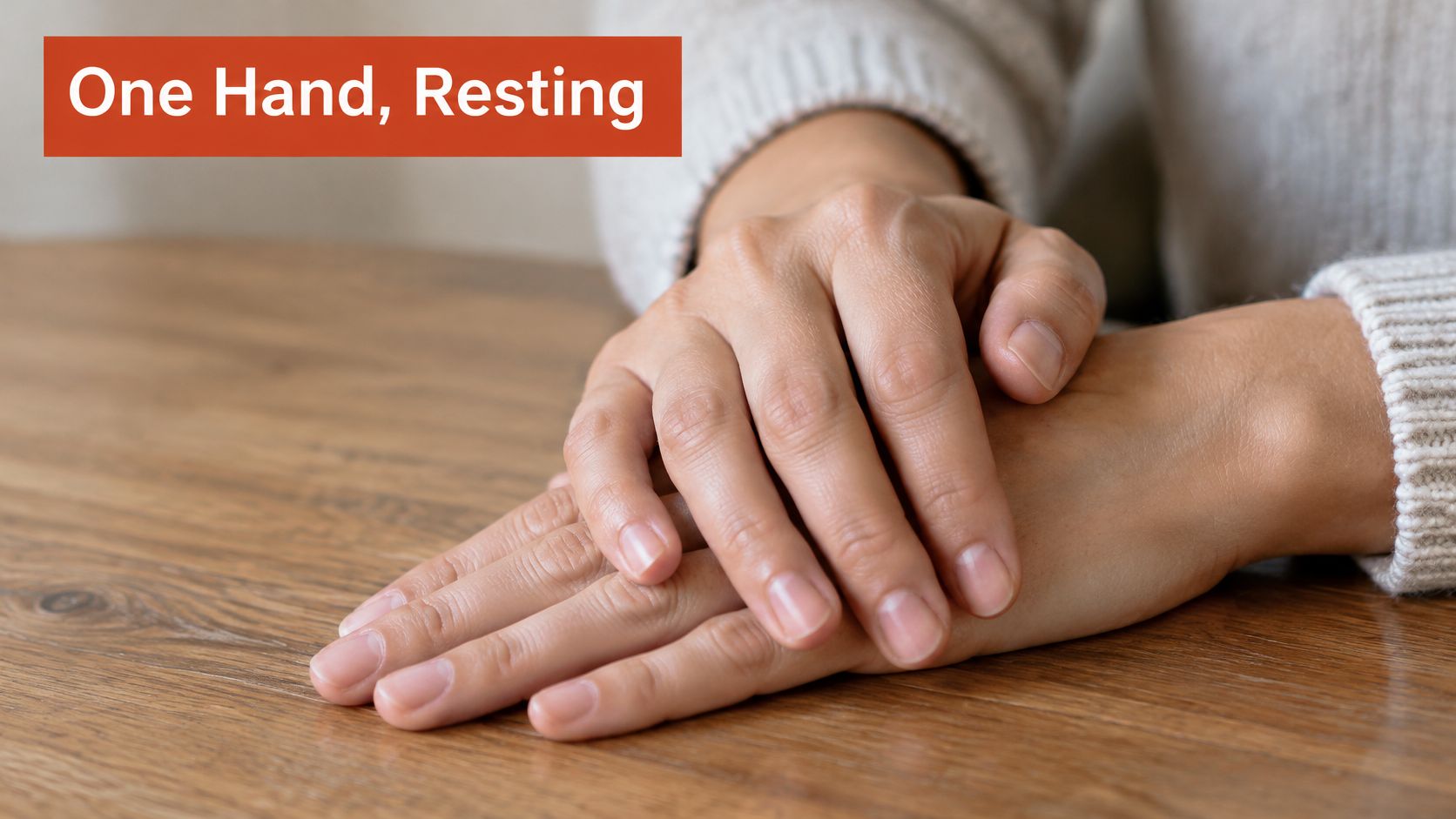 A close-up view of two hands resting gently on top of each other on a wooden table.