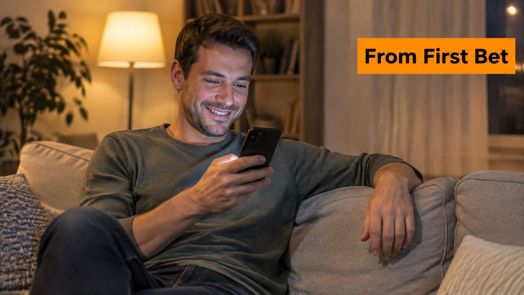 A happy man sitting on a comfortable sofa while looking at his smartphone in a cozy living room.