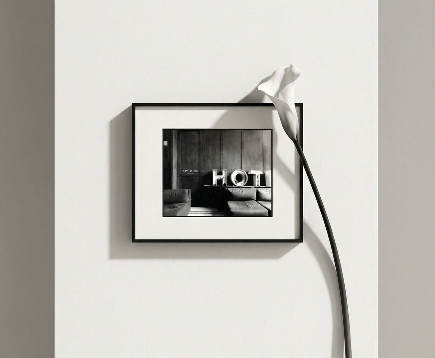 APHEUM Frame mit Schwarzweiß-Fotografie an einer hellen Wand, neben einer weißen Calla-Blüte.