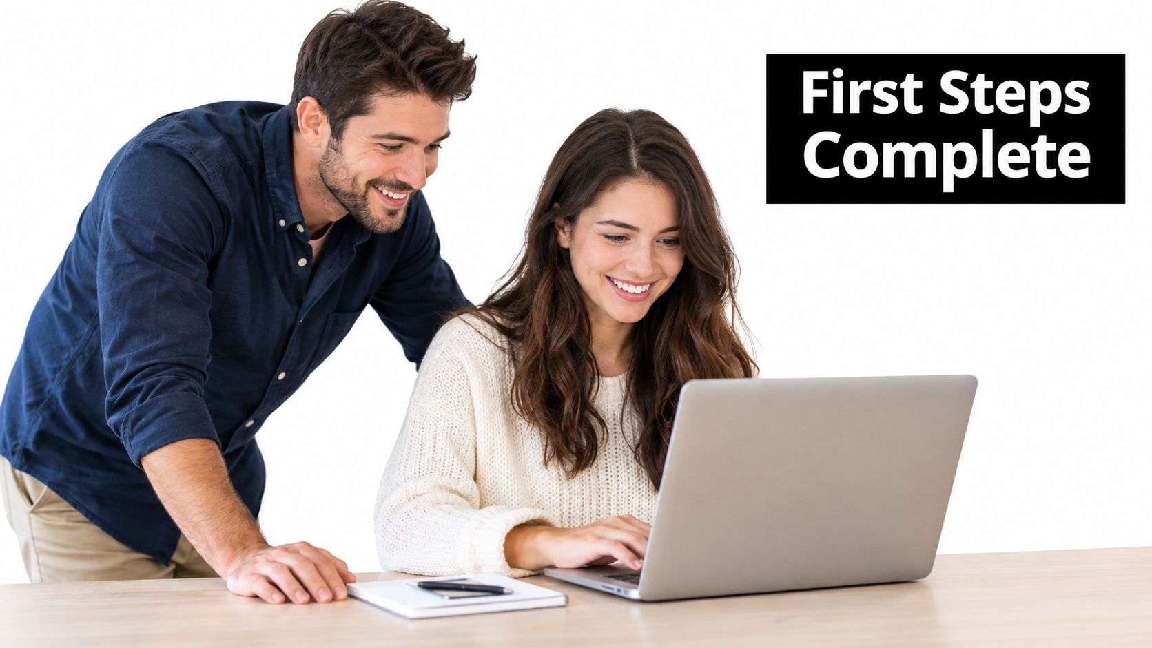 A man and a woman smiling while looking at a laptop computer together at an office desk.