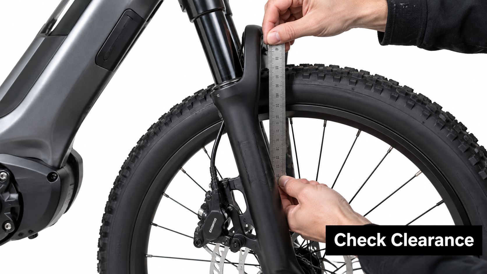 A close-up view of a person using a metal ruler to measure the tire clearance on an ebike fork.