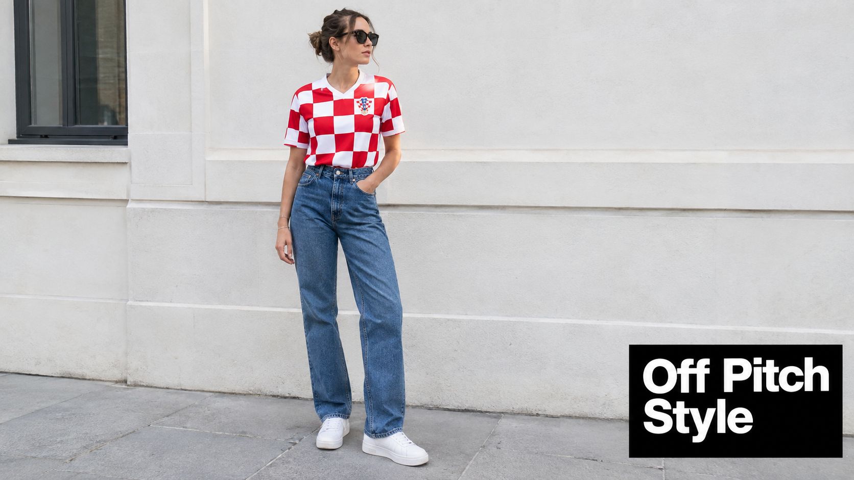 A stylish woman wearing a checkered Croatia soccer jersey with blue jeans and white sneakers standing outside.