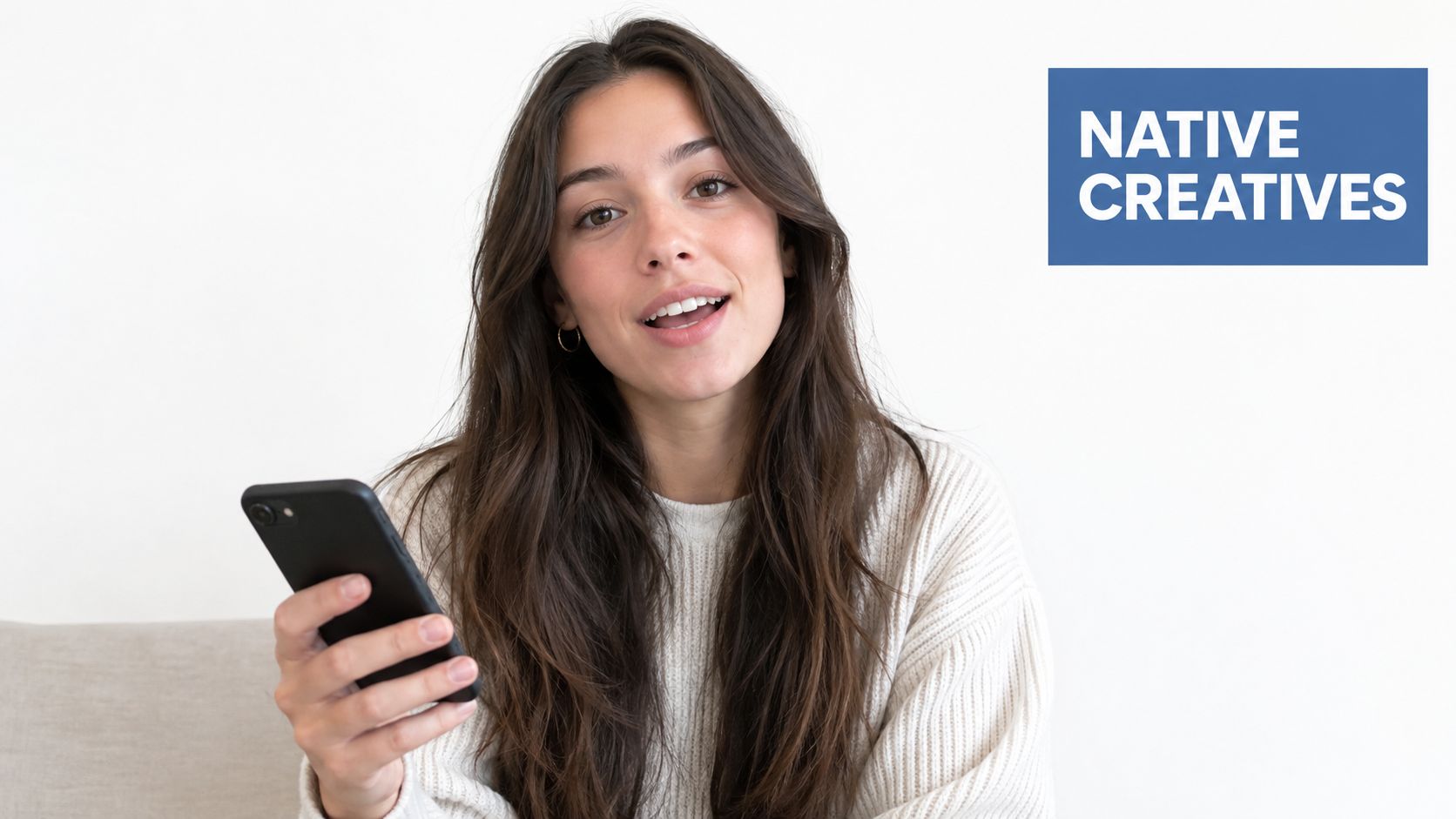 A young woman smiling while holding a smartphone in a bright, modern, minimalist studio setting.