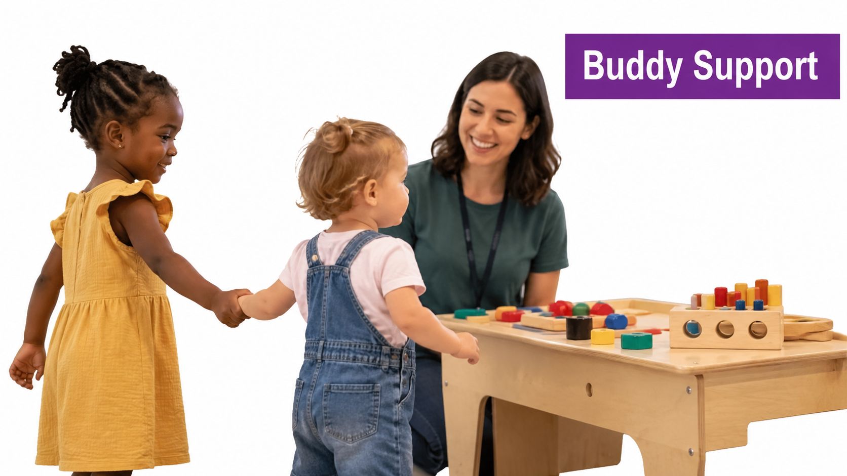 A teacher watches two young children holding hands while standing near a wooden activity table.