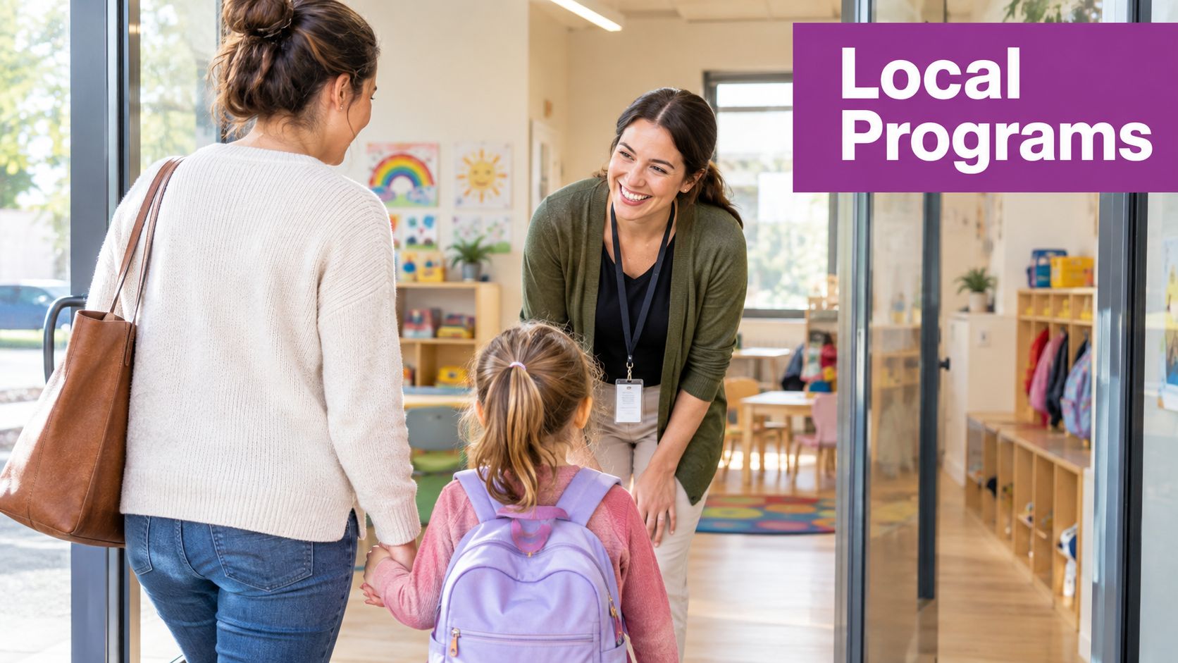 A teacher greets a young girl and her mother at the entrance of a colorful preschool classroom.