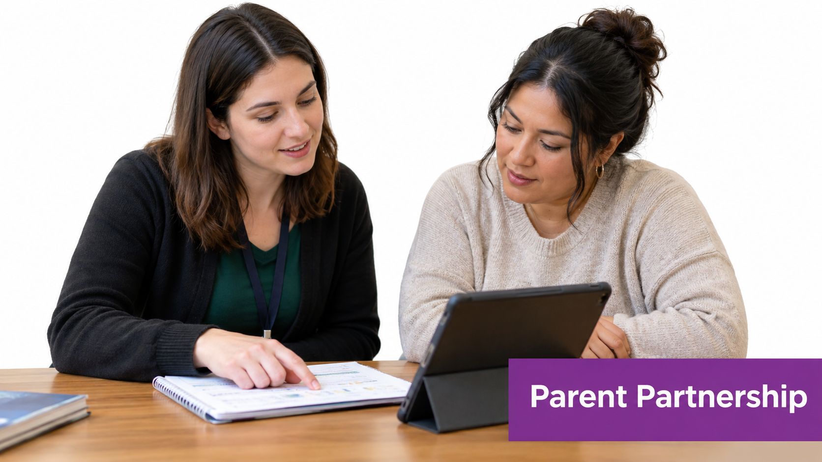 A teacher and a parent sitting together at a table discussing documents on a tablet.