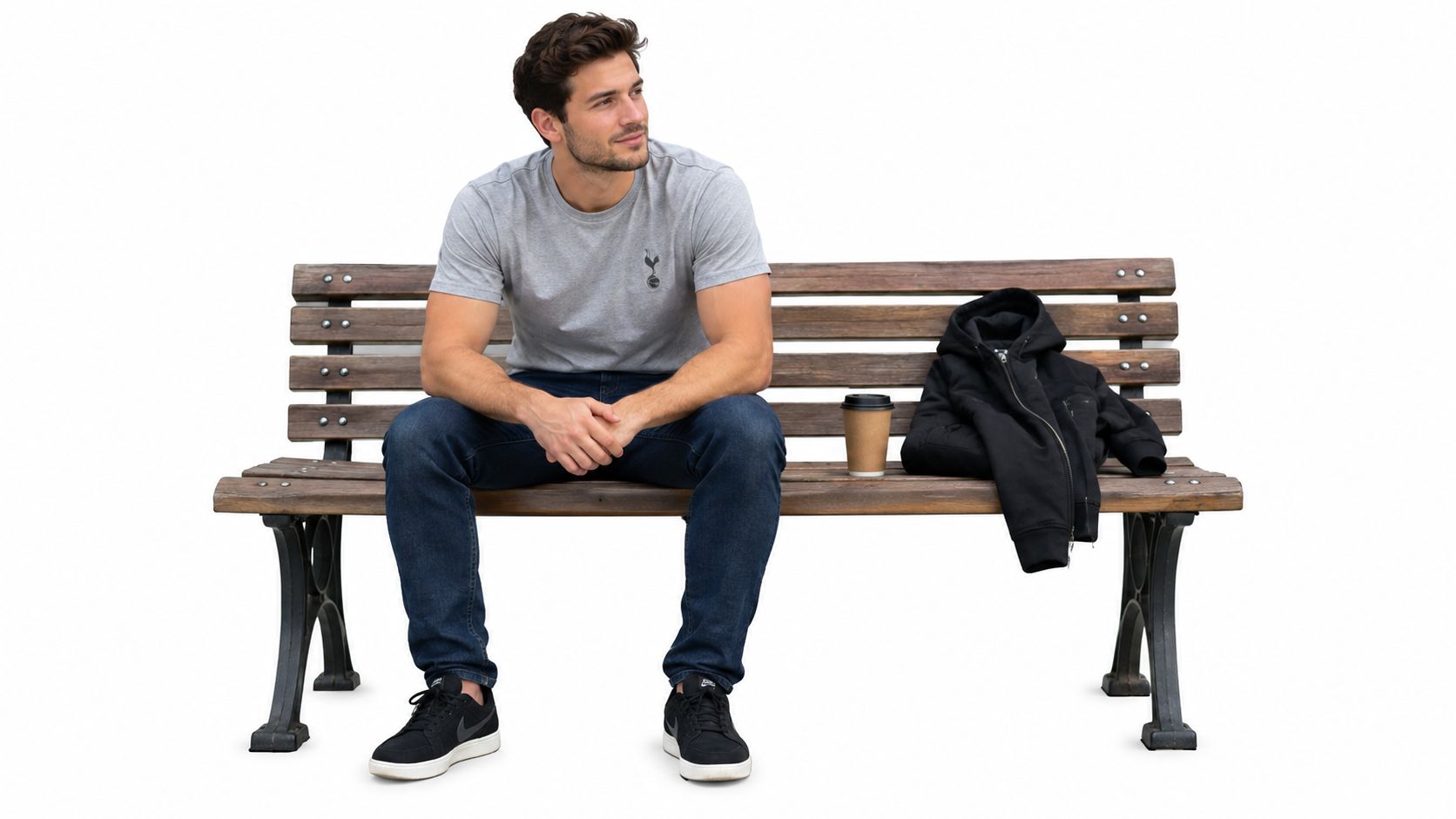 A man on a park bench displays a casual football fan outfit, including a t-shirt, jeans, sneakers, and jacket.
