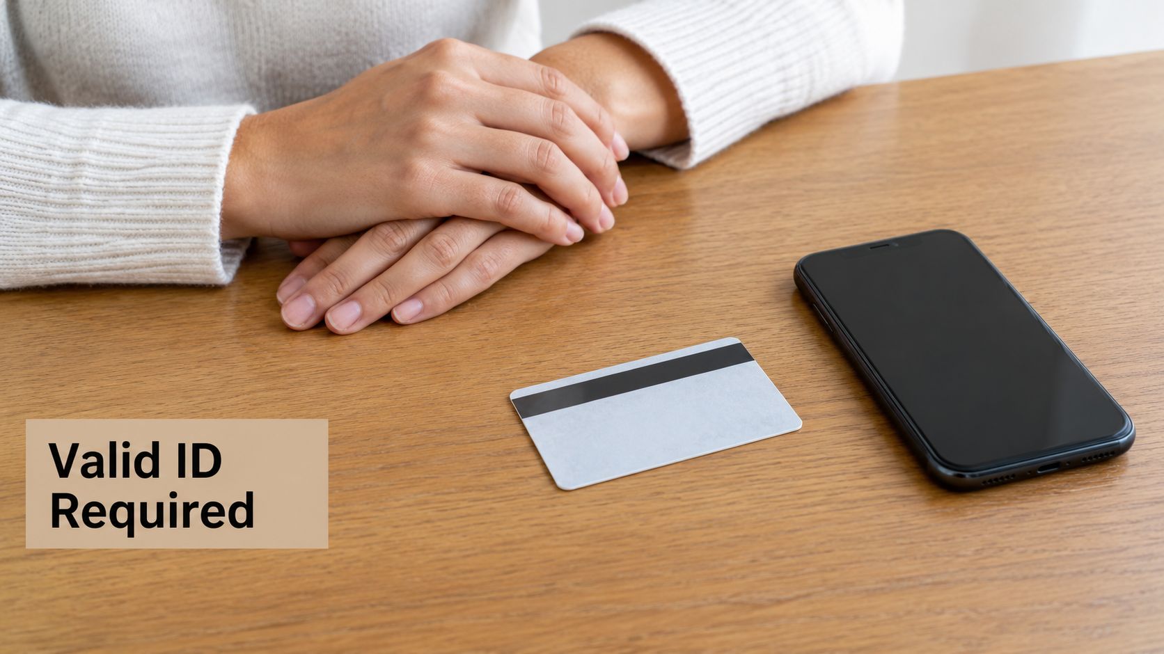 A person sitting at a desk with a smartphone and a payment card requiring valid identification.
