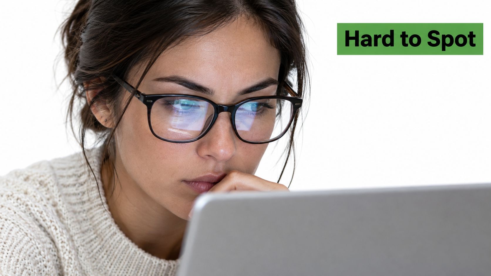 A young woman wearing glasses looking intently at a laptop screen with a focused expression.