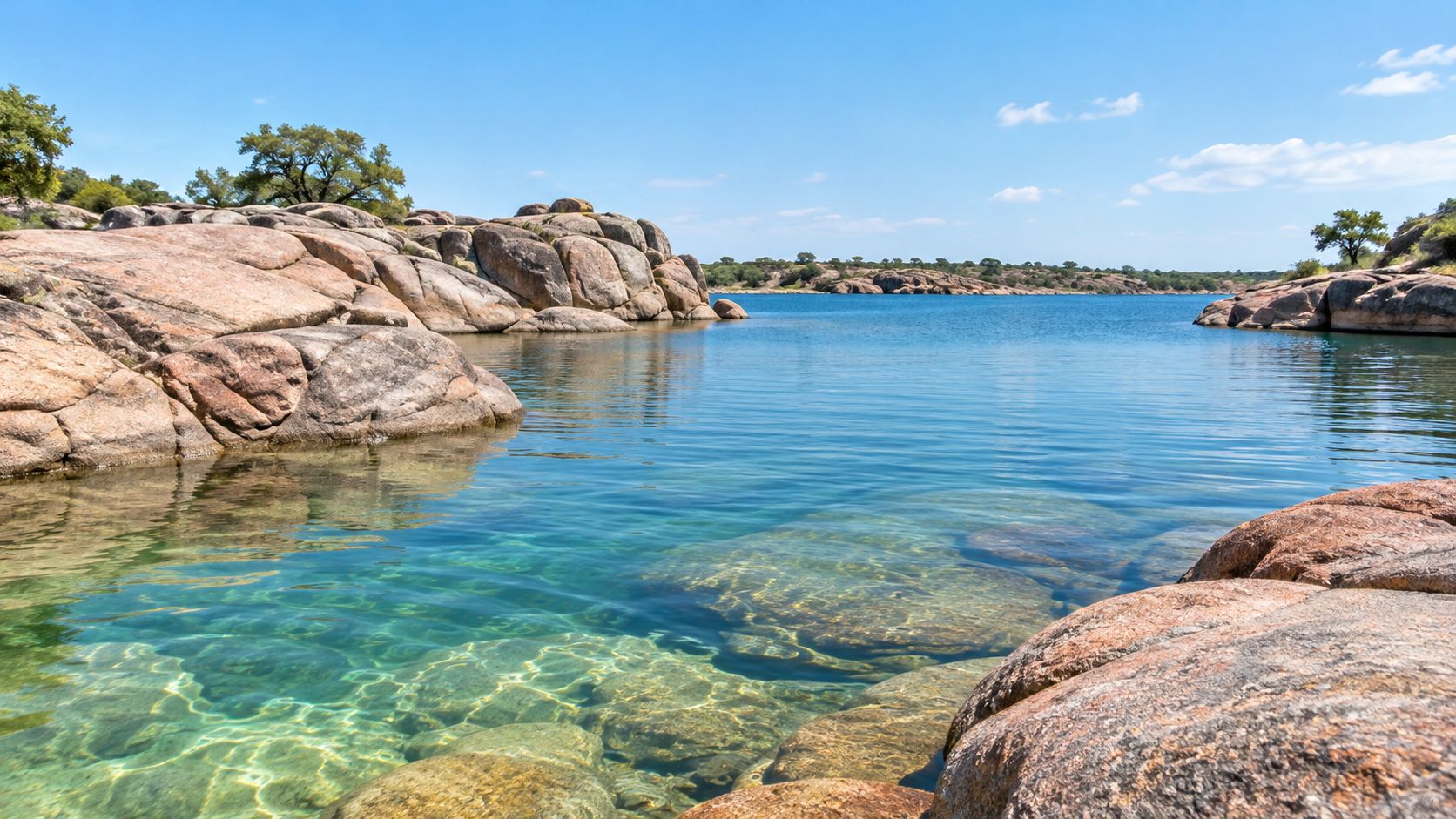 A serene, clear blue lake in Texas surrounded by weathered, light brown rock formations under a sunny sky.