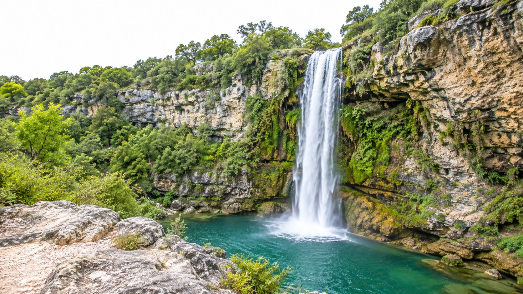 A tall Texas waterfall with vegetation growing along its rocky face.