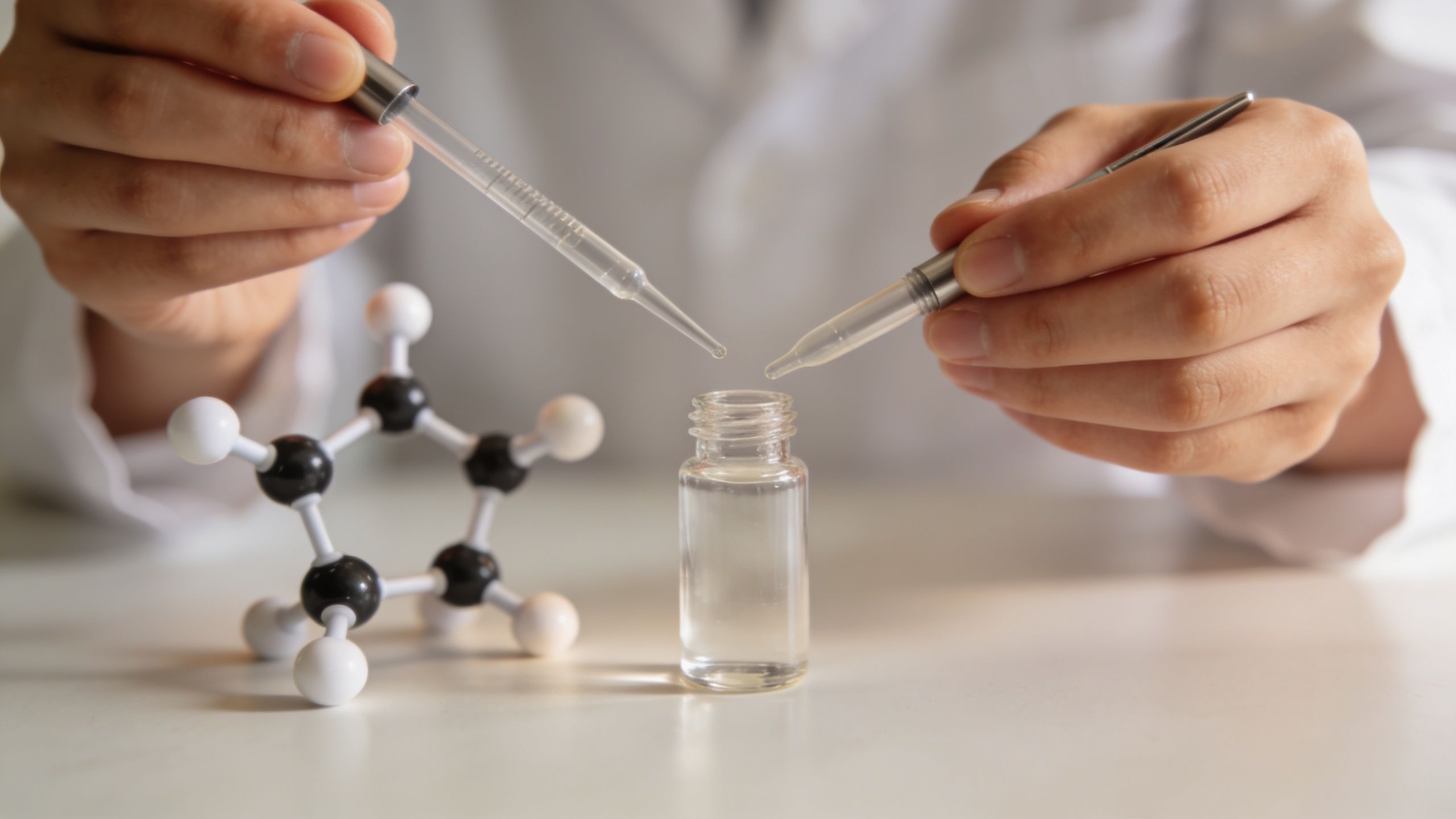 Vedecký pracovník v laboratóriu pracuje s chemickým modelom molekuly a malou sklenenou fľaštičkou s pipetou.