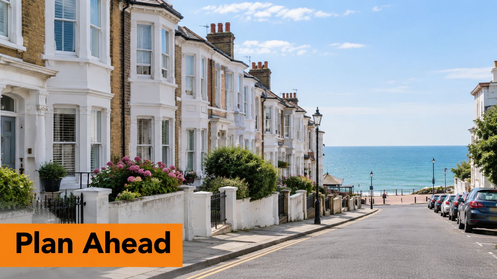 A scenic view looking down a coastal British street lined with terraced houses toward the blue sea.