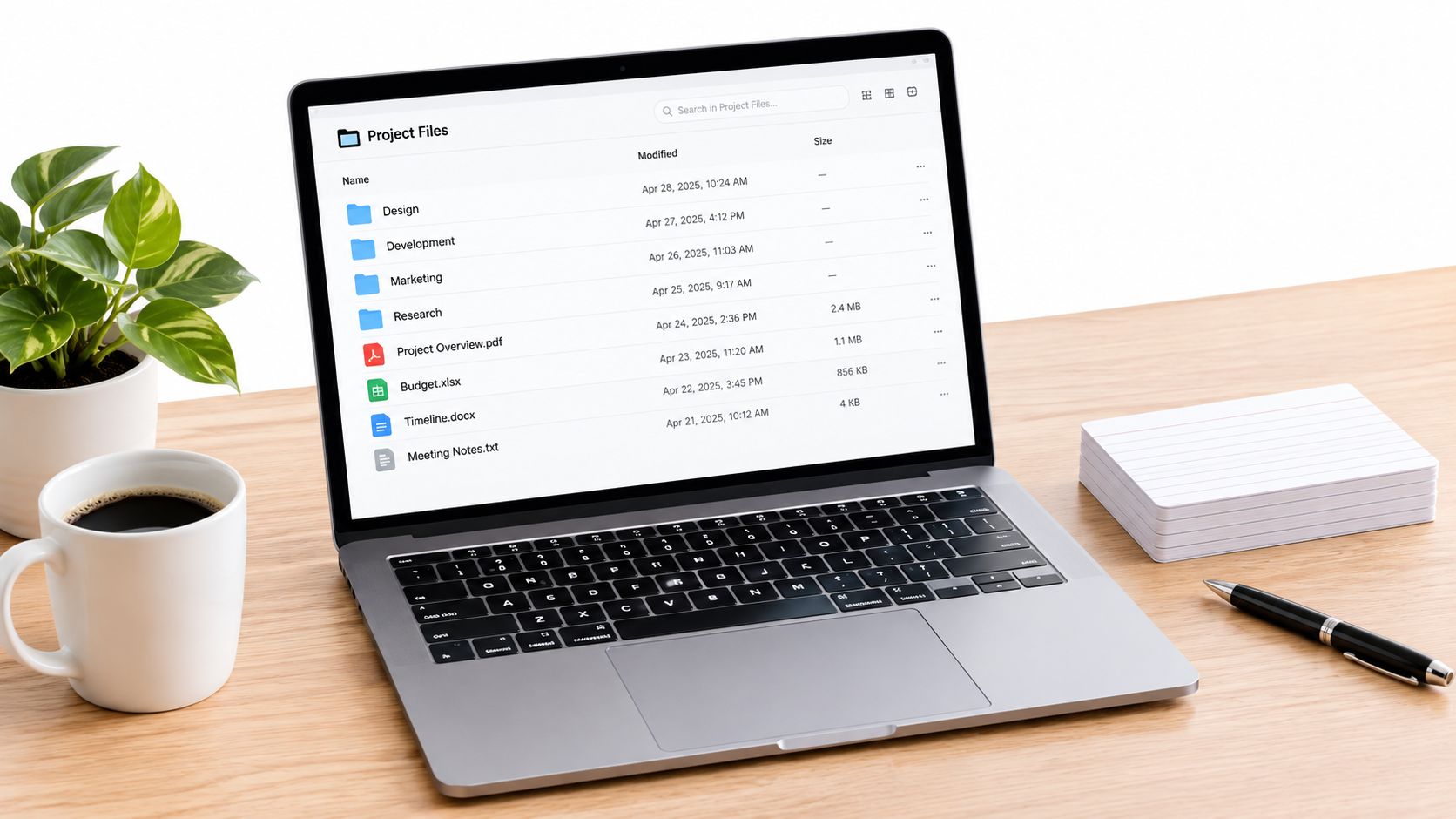 A modern laptop displaying project files on a clean office desk with a coffee mug and notebook.