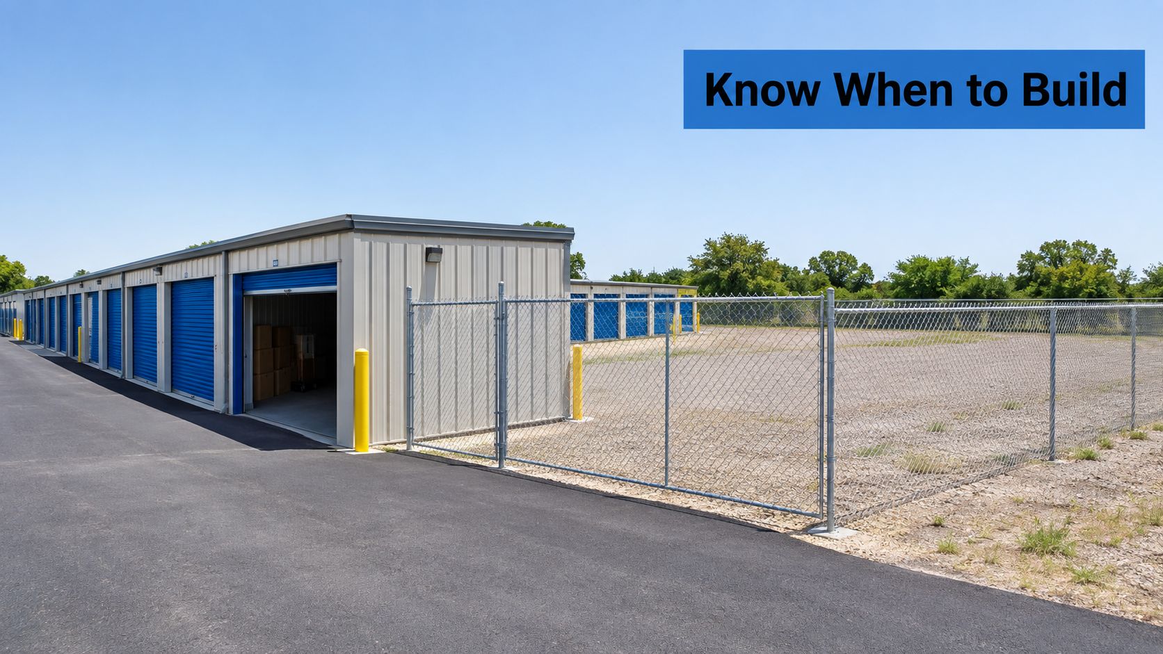 A row of self-storage units with blue roll-up doors next to a large fenced gravel development site.