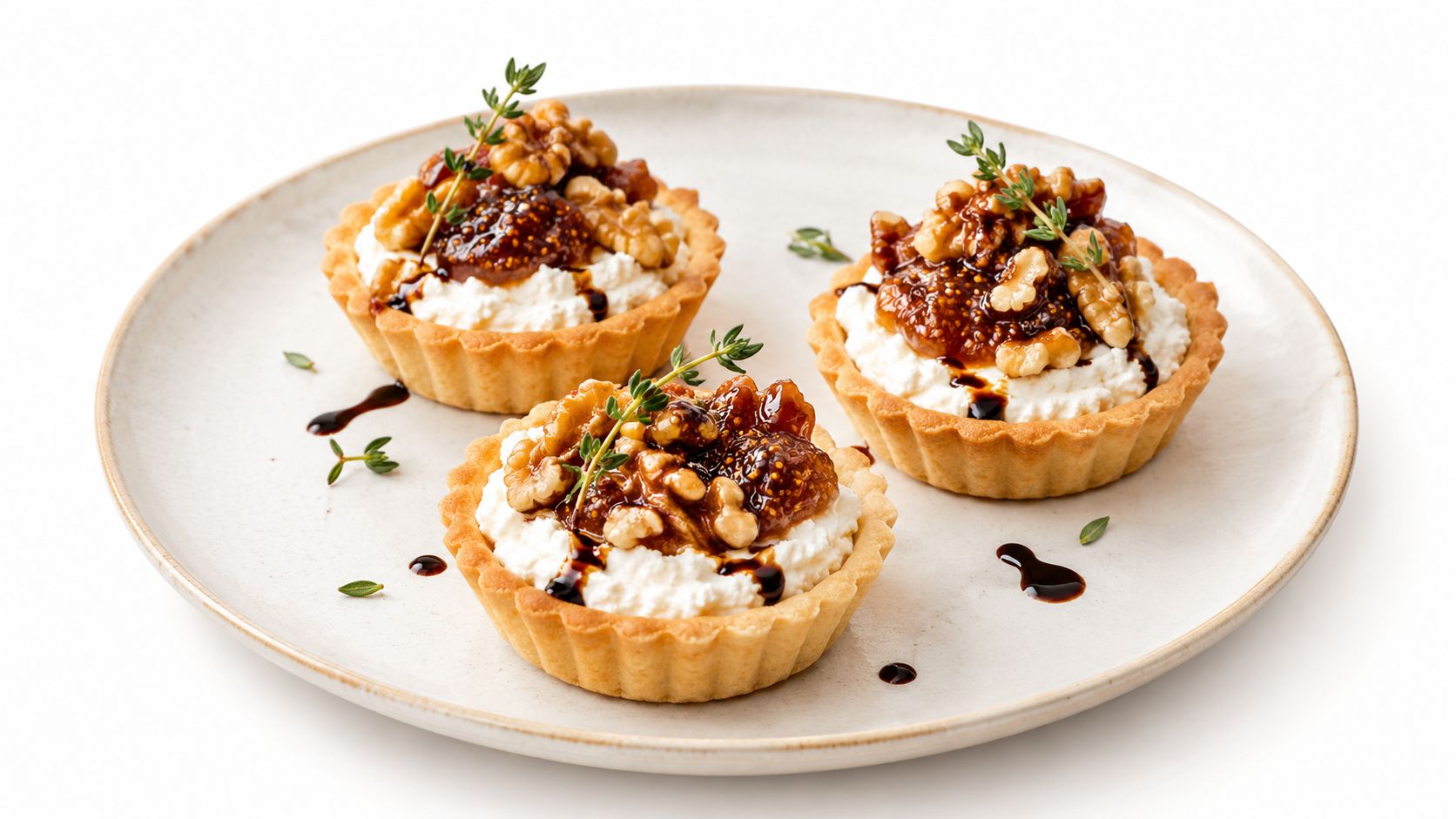 Three small savory tartlets topped with cream cheese, fresh figs, walnuts, and a balsamic glaze drizzle.