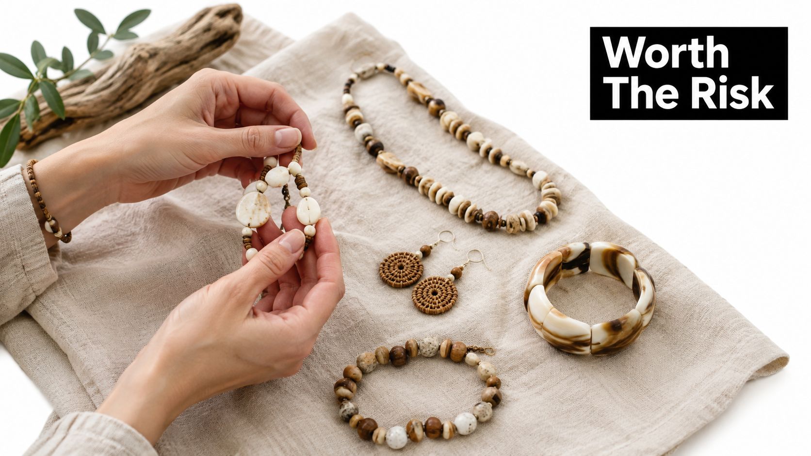 A person holding a beaded bracelet surrounded by various jewelry made from natural materials on linen fabric.