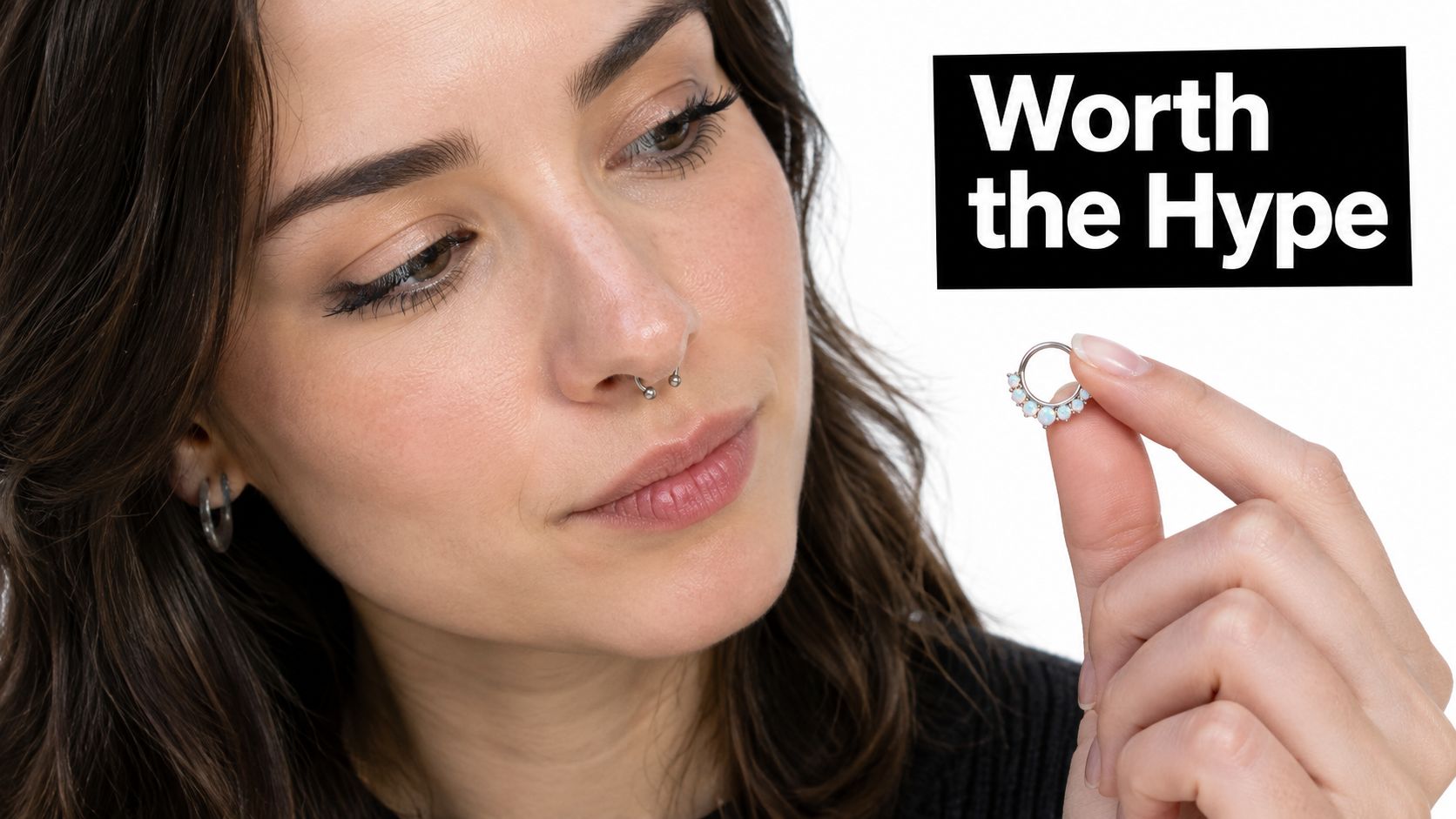 A woman looks closely at a small circular septum ring decorated with opal stones held in her fingers.